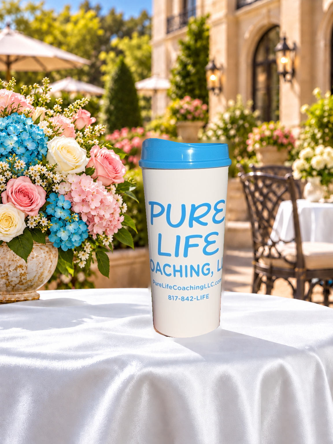 Pure Life Coaching LLC white travel mug with a blue lid, pictured on a table beside flowers